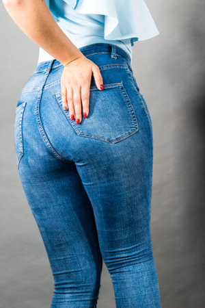Closeup of female plus size hips buttocks wearing blue jeans, woman presenting fashionable outfit. Fashion clothing femininity concept. Gray backgroundの写真素材