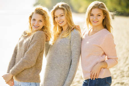 Three fashionable women wearing sweaters during warm autumnal weather spending their free time on sunny beach. Fashion models outdoorの写真素材
