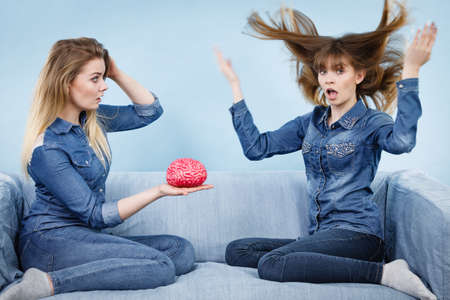 Friendship, human relations concept. Two women friends or sisters wearing jeans shirts, thinking about solving problem holding fake brain.の写真素材