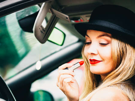 Young attractive woman looking in rear view mirror painting her lips doing applying make up while driving the car.の写真素材