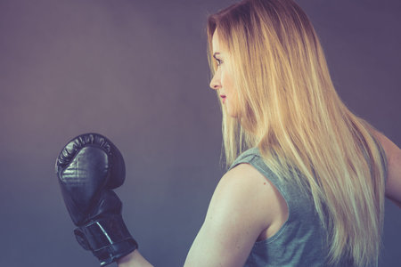 Sportsmanship fairplay and strong body. Young woman fighting boxing. Blonde girl wearing black punch gloves. Sport and fitness, power, exercising, on grayの写真素材