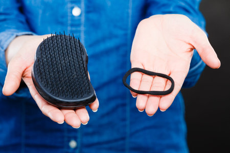 Everyday morning routine. Female hands with black comb hairbrush and elastic hair. Woman with barber equipment.の写真素材