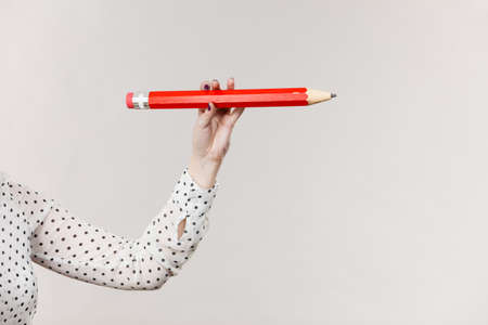 Education, stationery elements, school concept. Female hand student girl or business woman female teacher holding big red pencil. Studio shot on greyの写真素材