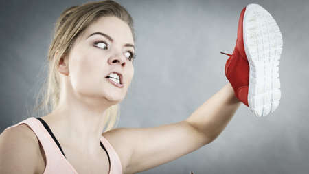 Furious woman holding red sport shoe being angry and mad at somebodyの写真素材