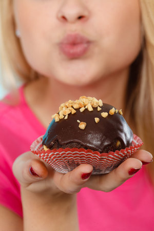 Diet, sweets, food concept. Woman holding delicious chocolate cupcake with peanut frosting about to...