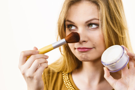 Fashionable cheerful young female holding professional powder brush, adding last touch to her make upの写真素材