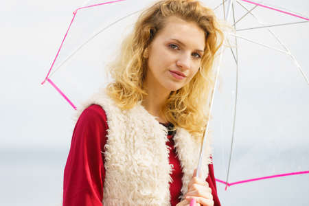 Pretty female wearing fur autumnal vest posing with transparent umbrella outdoor. Woman presenting autumn outfit.の写真素材