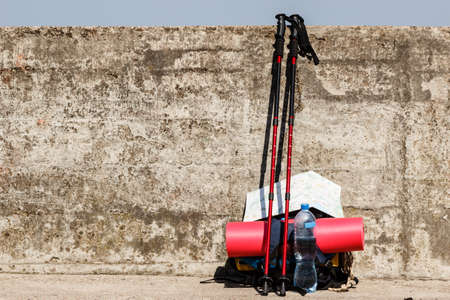 Equipment survival leisure trip holidays concept. Outdoor gear left outside. Bagpack map nordic walking sticks leaning on wall.の写真素材