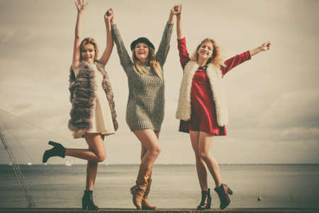 Three fashionable women having presenting pretty stylish outfits next to sea. Style, fashion, friendship concept.の写真素材