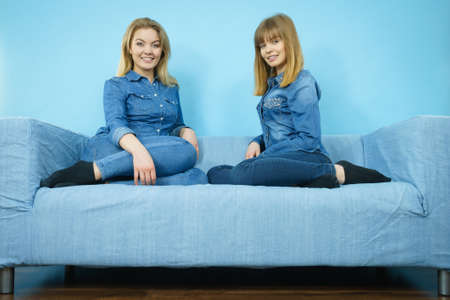 Friendship, human relations concept. Two happy women friends or sisters wearing jeans shirts sitting on sofa having fun.の写真素材