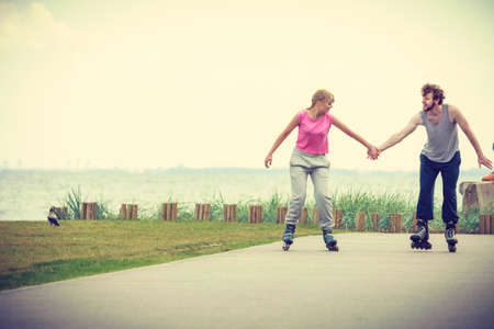 Active lifestyle people and freedom concept. Young fit couple on roller skates riding outdoors on sea coast, woman and man enjoying time together.の写真素材