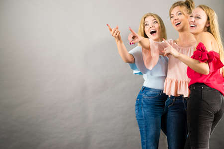 Fashionable adult female friends models pointing at grey copy space. Studio shotの写真素材