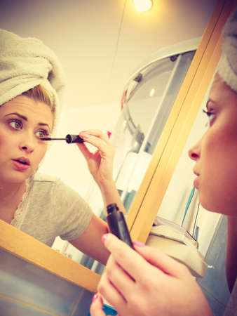 Visage and make up concept. Woman in bathroom wearing towel on head applying mascara on eyelashesの写真素材