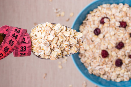 Diet healthy food weight loss concept. Oatmeal in blue bowl and pink measuring tape around spoon on...