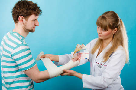 Corruption in healthcare industry. Female doctor bandaging male hand. Man giving money to woman. Bribery in medicine.の写真素材