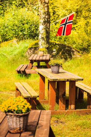 Norwegian flag and picnic site wooden table and benches outdoor in green forest park, Europe.の写真素材