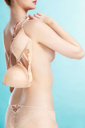 Bosom concept. Slim attractive naked woman holding beige plunge bra in hand, on blueの写真素材