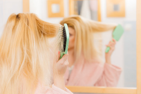 Woman wearing dressing gown brushing her long blonde hair, morning beauty routine. Haircare and hairstyling concept.の写真素材