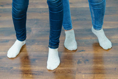 Women feet standing on wooden floor wearing blue jeans and light socks.の写真素材