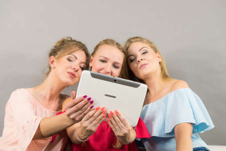 Women sitting on sofa having fun surfing on the internet using smart digital pc tablet modern deviceの写真素材