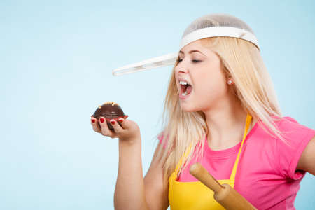 Baking tasty desserts sweets at home concept. Woman holding delicious sweet chocolate cupcake wearing apron and colander on head as hat.の写真素材