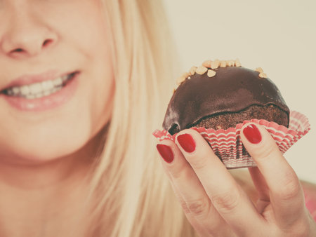 Diet, sweets, food concept. Woman holding delicious chocolate cupcake with peanut frosting about to...