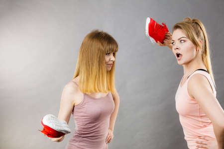Two agressive women having argue fight using shoes being mad at each other. Female violance concept.の写真素材