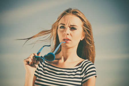 Summer relaxation concept.. Portrait girl with blue heart shaped sunglasses enjoying summer breeze outdoor on sky backgroundの写真素材
