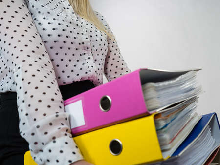 Woman holding many heavy colorful binders with documents. Office, bookkeeping objects concept.の写真素材