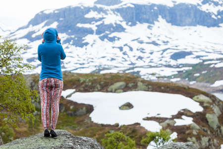 Travel, freedom. Tourist woman looking at landscape, mountains covered with snow in Norwayの写真素材