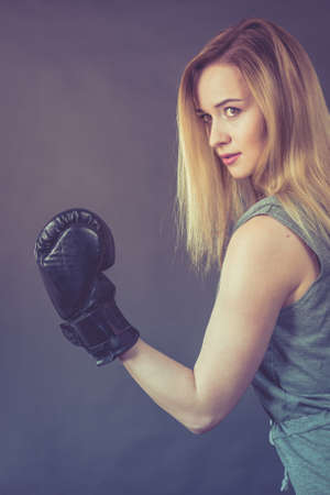 Sportsmanship fairplay and strong body. Young woman fighting boxing. Blonde girl wearing black punch gloves. Sport and fitness, power, exercising, on grayの写真素材