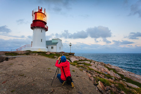 Female tourist traveler taking photo at historic red white lighthouse on the edge of rocky sea...