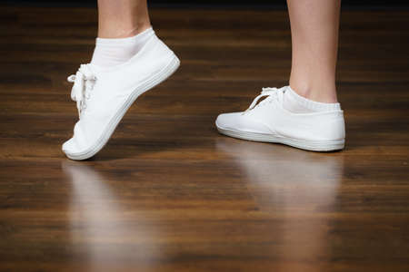 Unrecognizable woman wearing white bright sneakers trainers and socks standing on shiny wooden floor.の写真素材