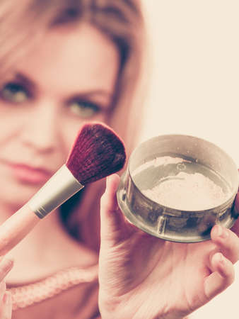 Fashionable cheerful young female holding professional powder brush, adding last touch to her make upの写真素材