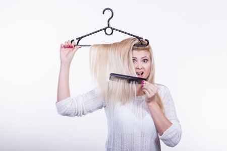 Hairstyle and haircare concept. Blonde woman with hair in clothes hanger and brushing