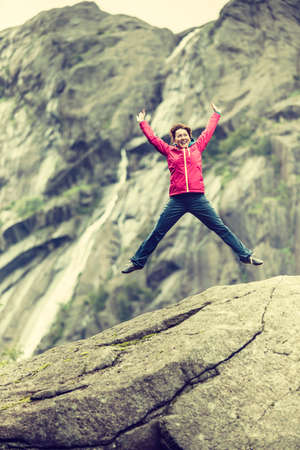 Happy woman jumping on rock in grey mountains, enjoying traveling and adventure.の写真素材