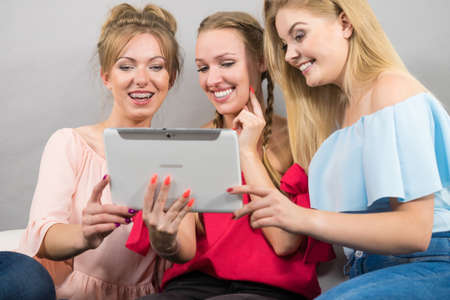 Women sitting on sofa having fun surfing on the internet using smart digital pc tablet modern deviceの写真素材