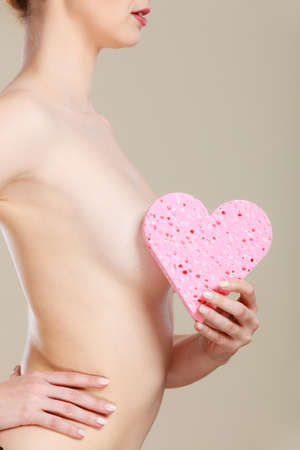Skincare hygiene medicine and body treatment. Sensual naked woman with beautiful figure perfect skin holding pink heart shaped sponge in hands.の写真素材