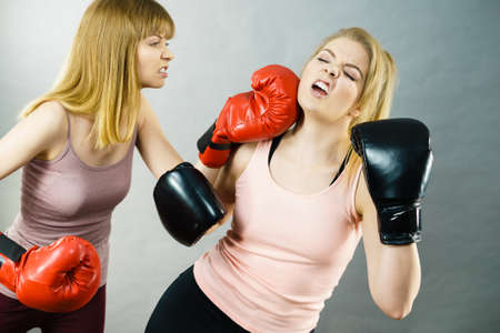 Two agressive women wearing boxing gloves having argue fight being mad at each other. Female violance concept.の写真素材