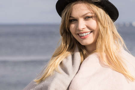 Beautiful young blonde woman wearing fedora hat, long warm fur sweater jumper outdoorの写真素材