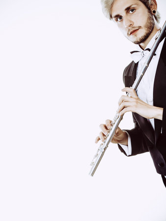 Classical music study concept. Male flutist musician performer playing flute. Young elegant man wearing tailcoat holds instrumentの写真素材