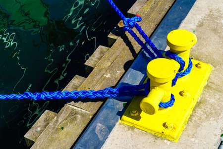 Shipping objects concept. Sailing ropes tied around yellow marina bollard. Outdoor shot on sunny day.の写真素材