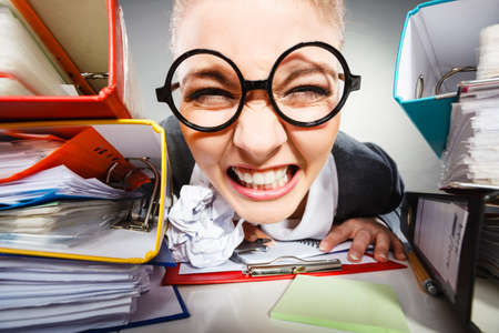 Workaholism mental insanity weird job work company concept. Insane office woman at work. Mad secretary making silly expression lurking through her desk.の写真素材