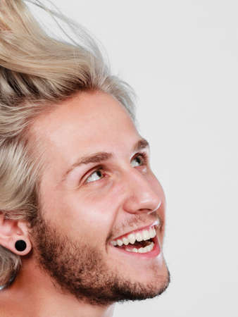 Fashion, hairstyle, happiness, joy concept. Happy smiling blonde man wearing grey t shirt, close up studio shot grey backgroundの写真素材