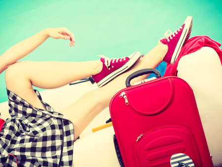 Traveling, waiting for adventure concept. Woman relaxing lying on sofa after packing clothes into her red suitcase. Indoor shotの写真素材
