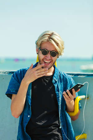 Contacts, technology concept. Young blonde man on vacations using his smartphone to check social media.の写真素材