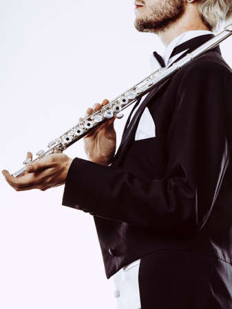 Classical music study concept. Male flutist musician performer playing flute. Young elegant man wearing tailcoat holds instrumentの写真素材