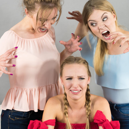 Woman being bullied by her two female friends. Women having argument. Angry fury girls screaming at her friend or younger sister. Friendship difficulties, rivaly and envy problems.の写真素材