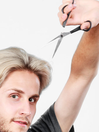 Hairstyle and haircut. Young cool guy barber holding shears tool ready to hair trimming. Blonde male with scissors creating new hairdo coiffureの写真素材