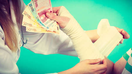 Corruption in healthcare industry. Female doctor bandaging male hand. Man giving money to woman. Bribery in medicine.の写真素材